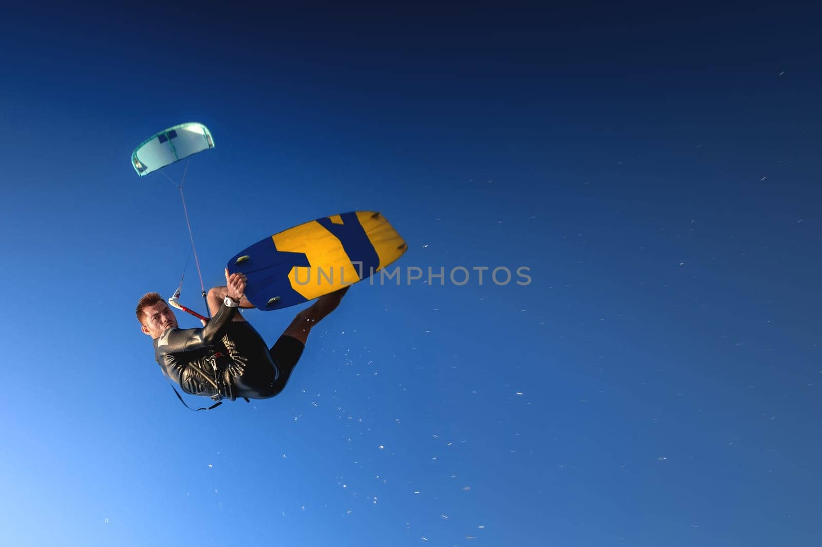 A kitesurfer rides while suspended in the air. Kitesurfer jumps against a beautiful blue sky background catching his board in the air.