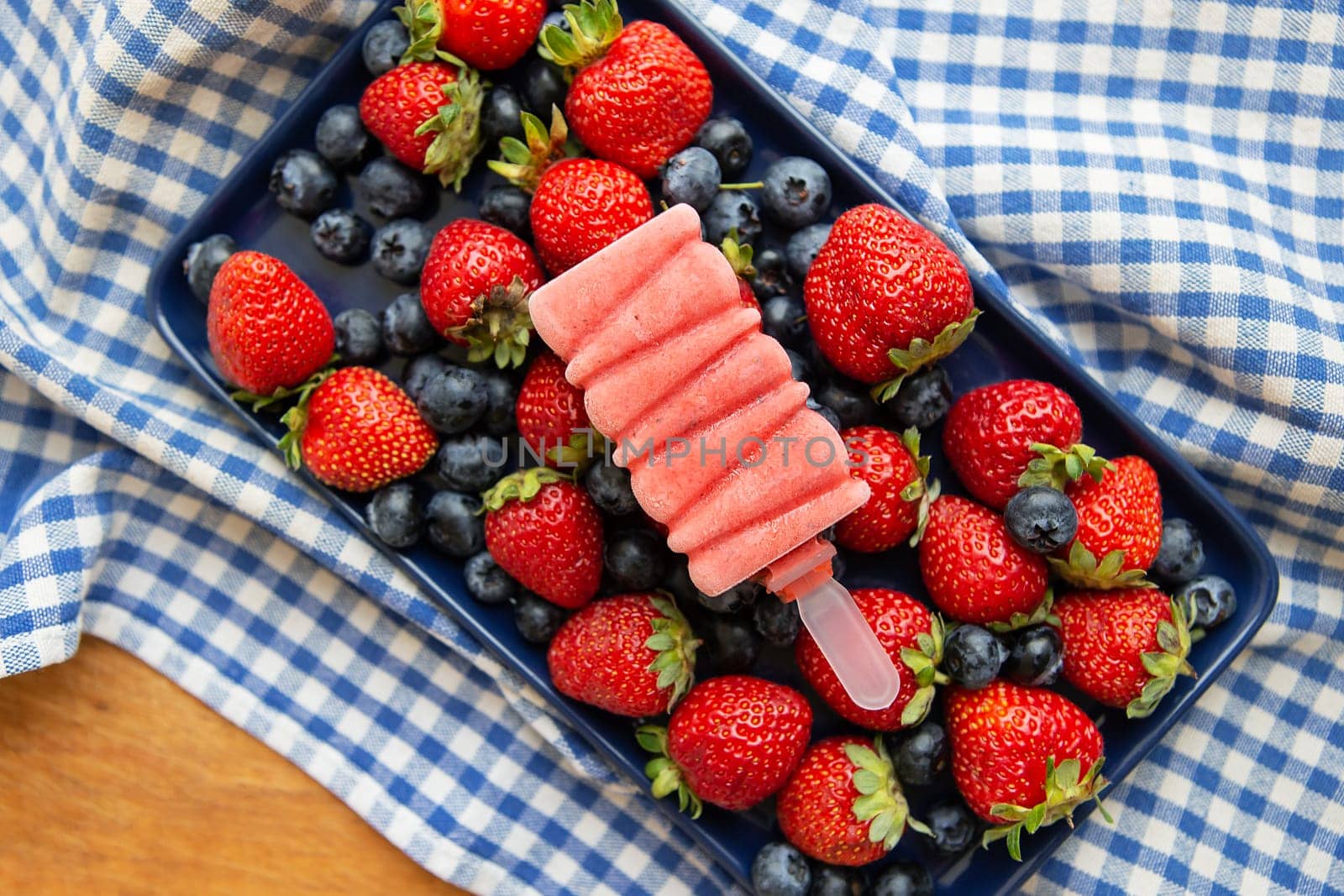 Delicious ice cream from fresh strawberries and blueberries close-up lies on fresh strawberries and blueberries. Blue check napkin