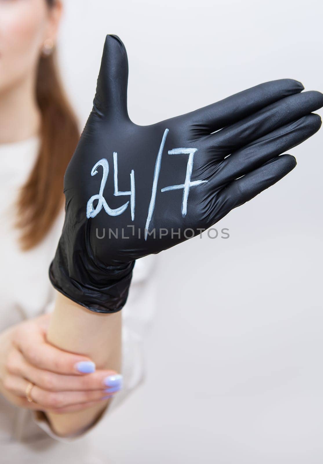 A woman's hand in a black rubber glove on which is written 24 7, help at any time, always in touch. Support and help concept. by sfinks