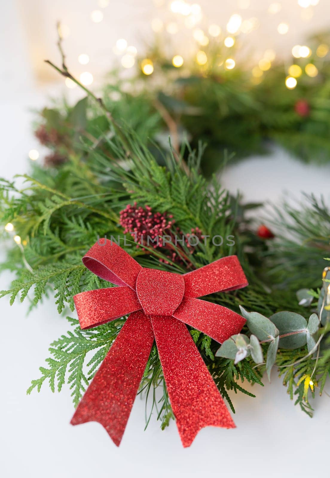 Stylish indoor Christmas wreath with a beautiful red bow, hang the wreath on the door. Festive atmosphere, beautiful bokeh in the background