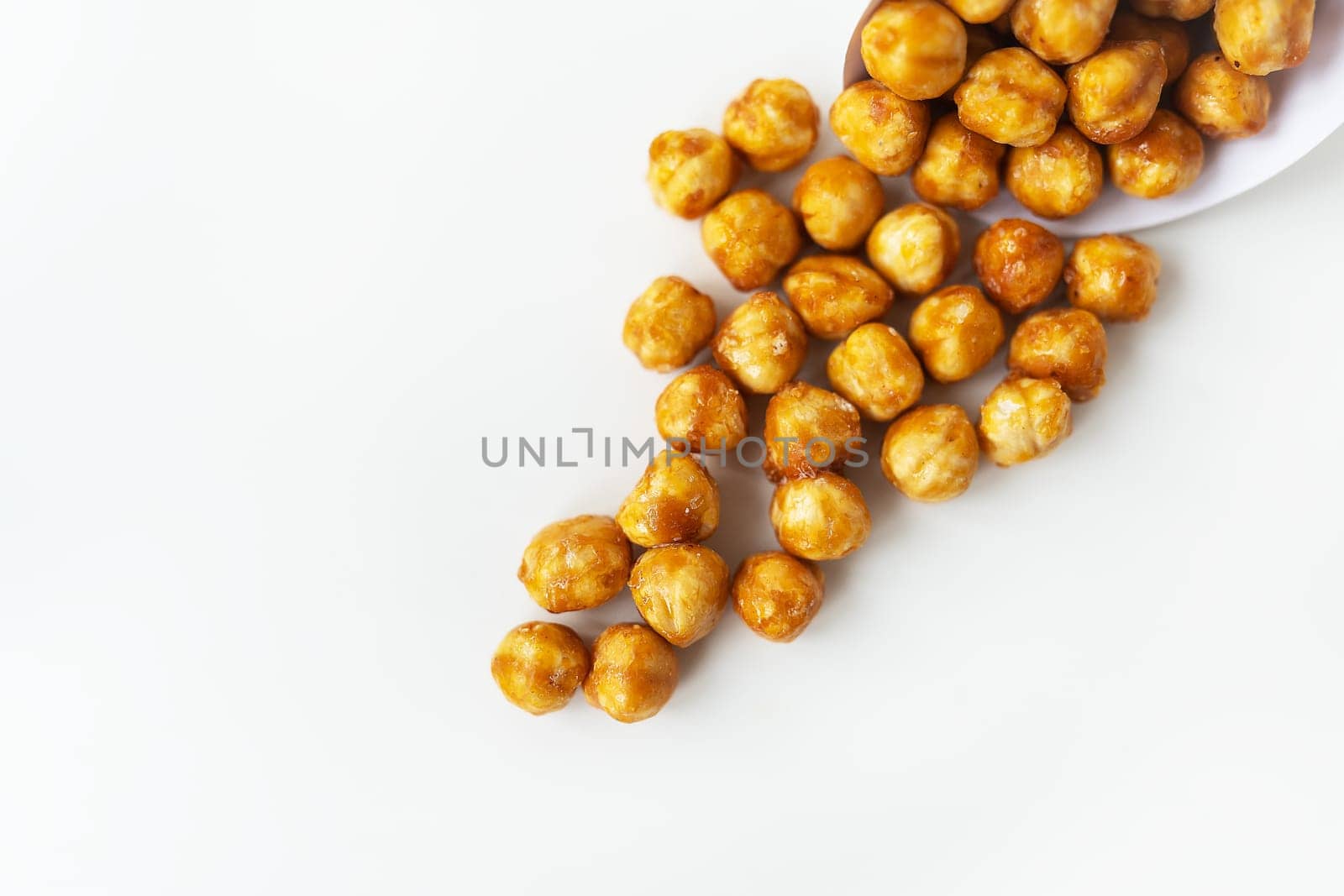 Scattered hazelnuts in caramel on a white background. Very tasty and healthy and high-calorie dessert