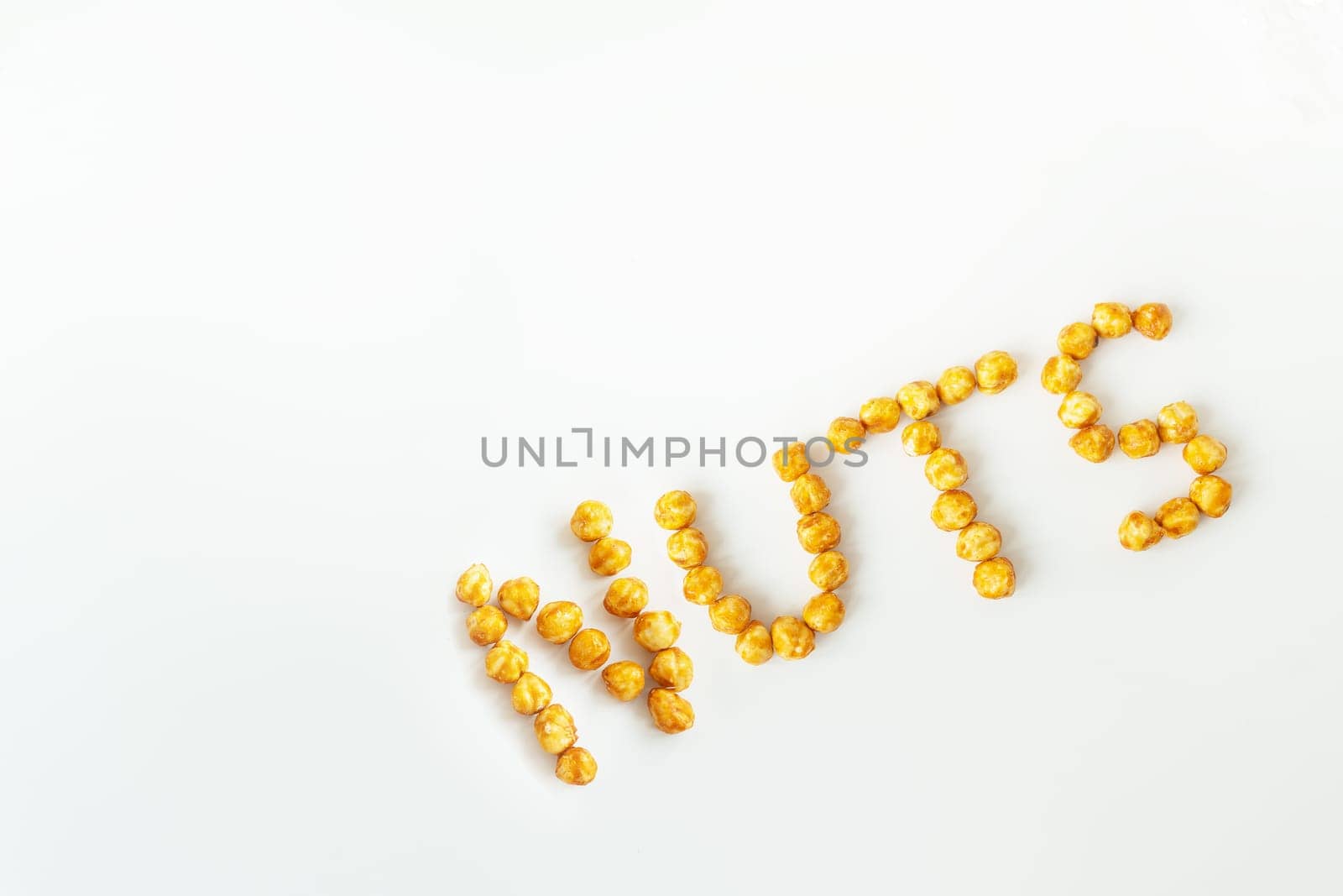Scattered hazelnuts in caramel on a white background. Very tasty and healthy and high-calorie dessert. Walnut inscription