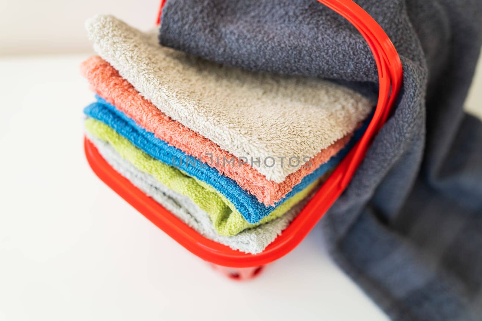 Multi-colored towels lie in a red laundry basket on a white background. Washing and ironing clothes, top view