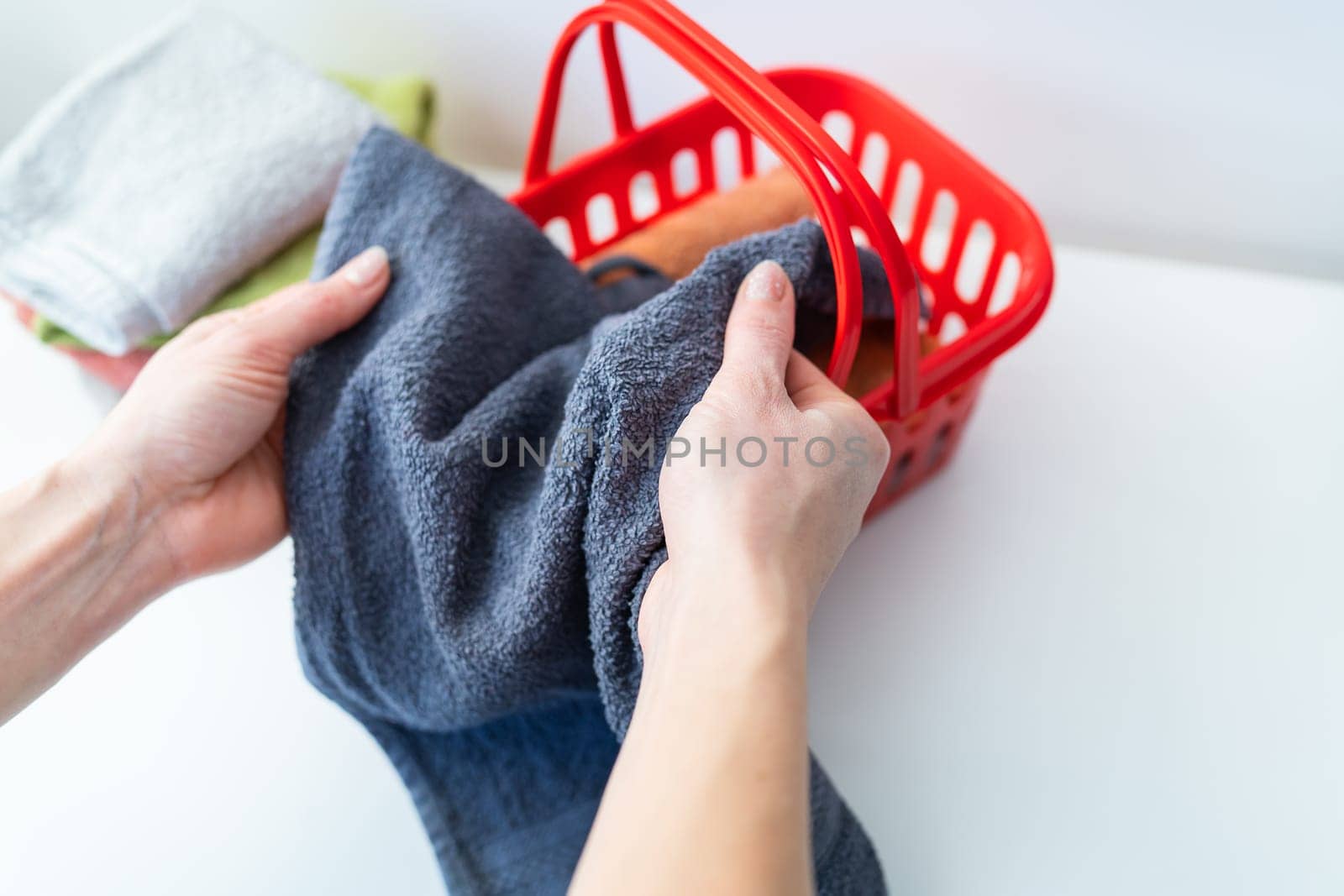 Multi-colored towels lie in a red laundry basket, a woman folds a towel. Laundry and ironing