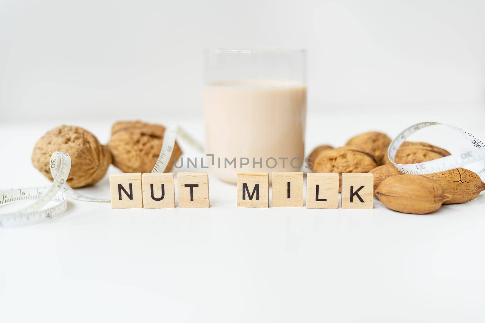 Vegan milk from nuts in a glass cup with various nuts on a white table. Lettering nut milk
