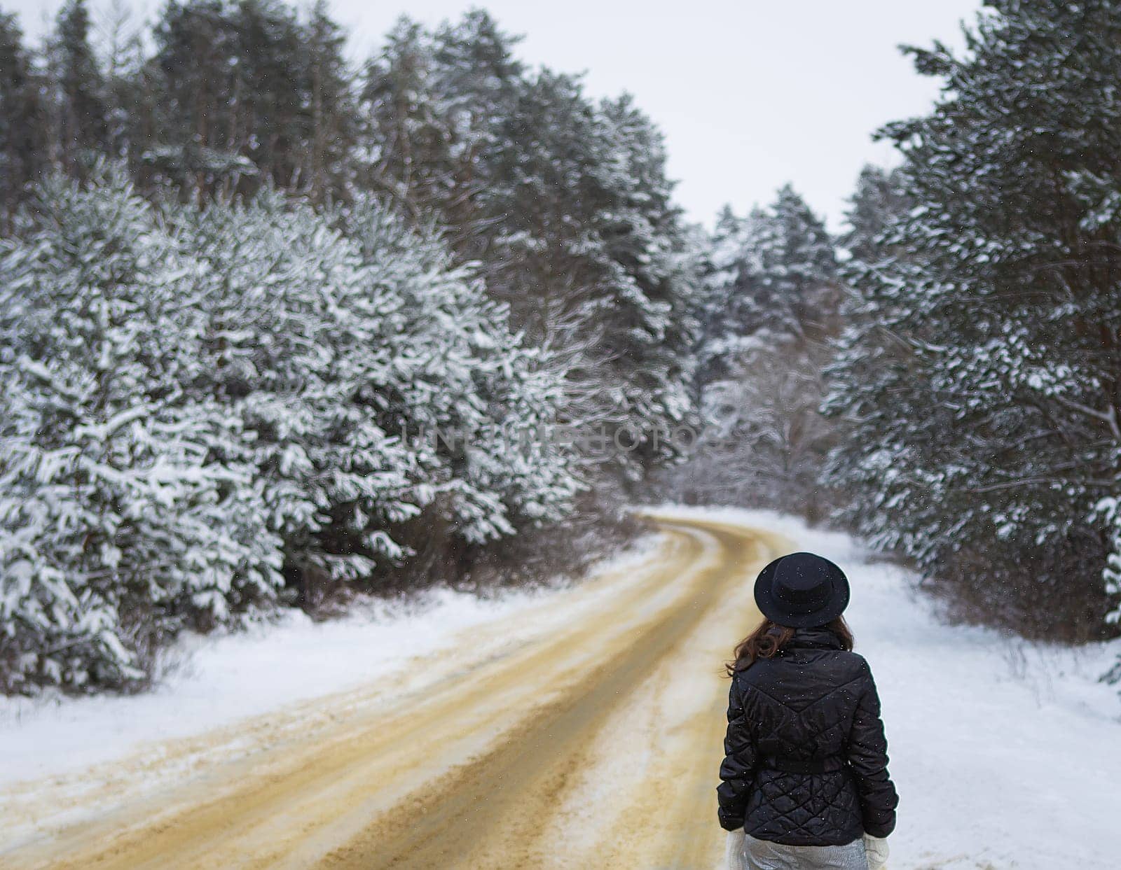 Beautiful snowy day, blizzard. The girl stands with her back in the middle of the road in a dense pine forest. Noise and grain effect