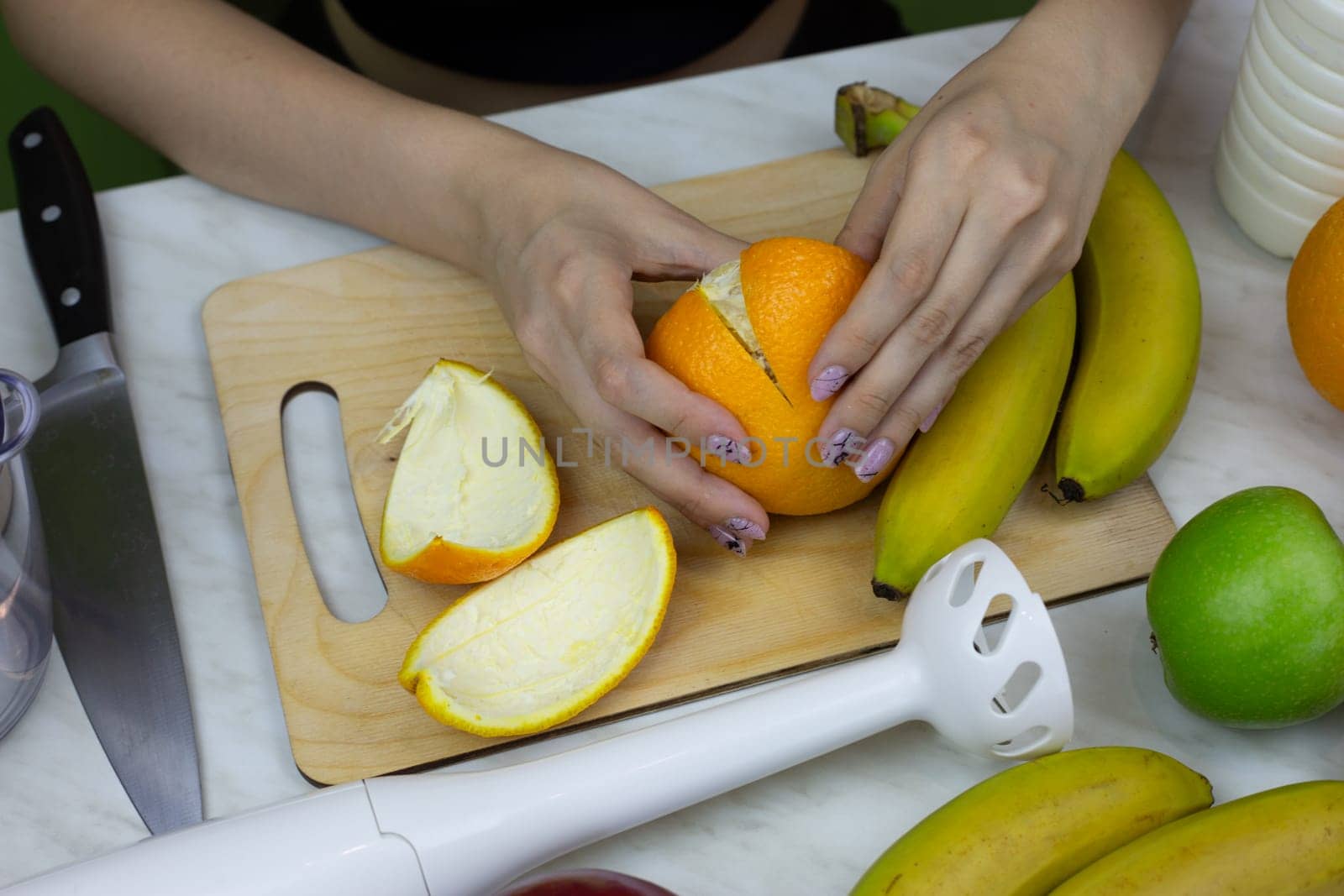 Girl peels an orange while making healthy drink in blender. Homemade sports fruit cocktail to improve health and boost vitamins