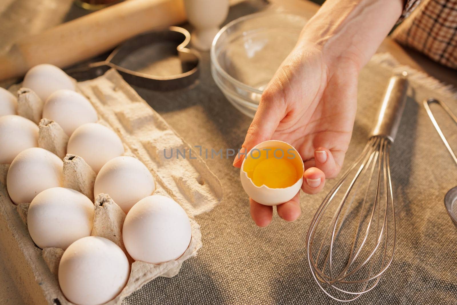 Close-up of female hands holding broken chicken egg on kitchen table background, egg carton, dough preparation