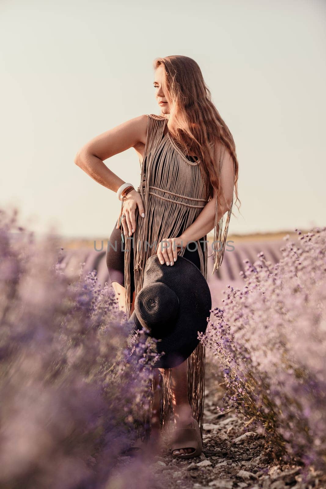 A woman is standing in a field of purple flowers, wearing a black dress and a black hat