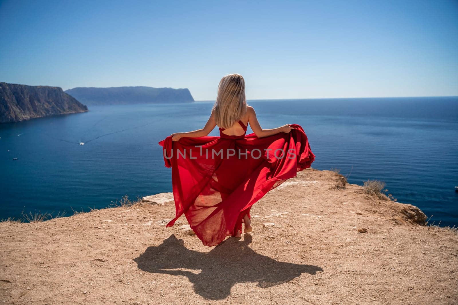 A woman in a red dress stands on a cliff overlooking the ocean. The scene is serene and peaceful, with the woman's dress adding a touch of elegance to the landscape