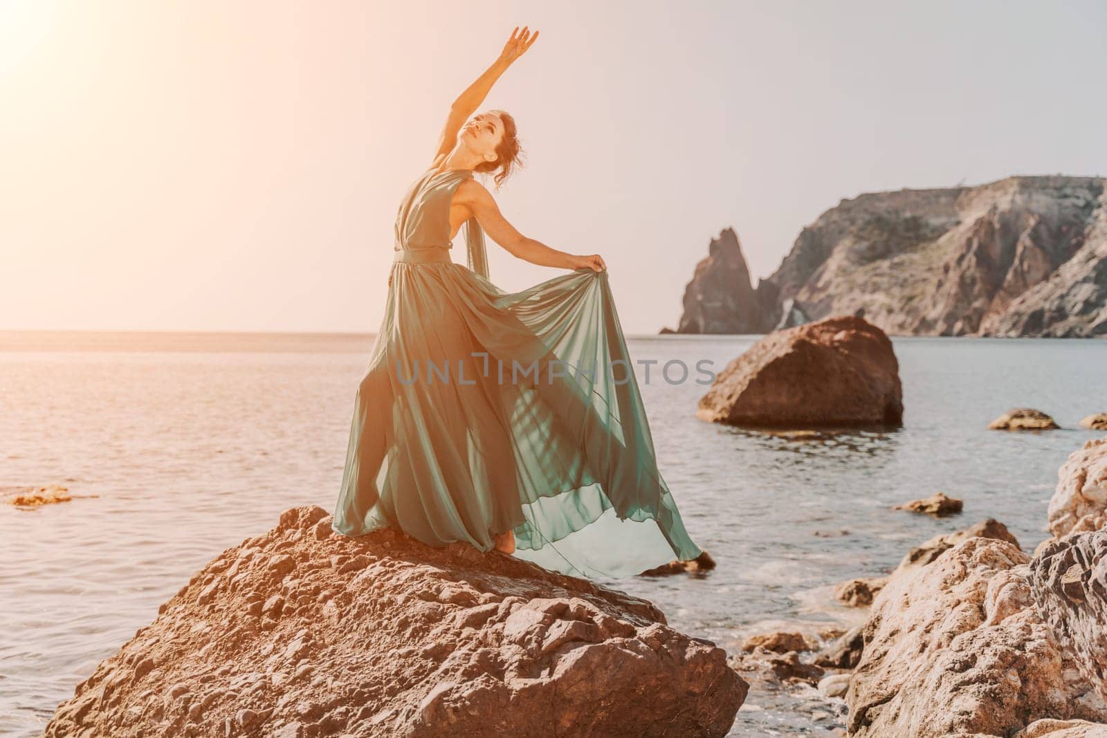 Woman green dress sea. Woman in a long mint dress posing on a beach with rocks on sunny day. Girl on the nature on blue sky background