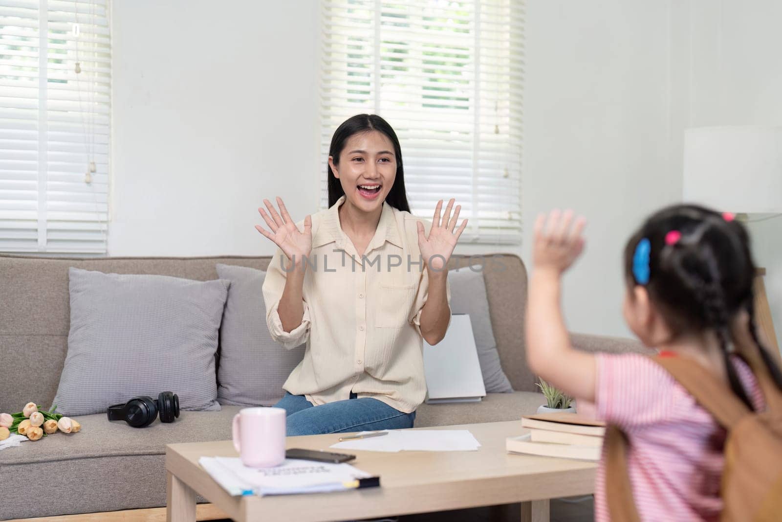 Asian mother waves playfully to her daughter, creating a encouraging and warm morning routine before school.