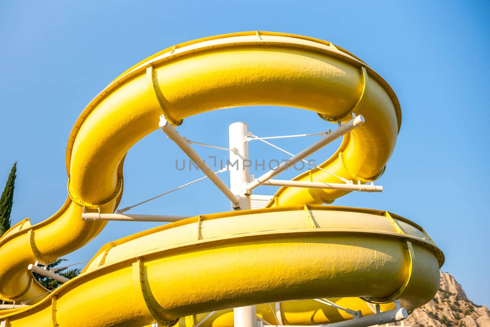 A yellow waterslide curves through the air against a bright blue sky. family vacation concept