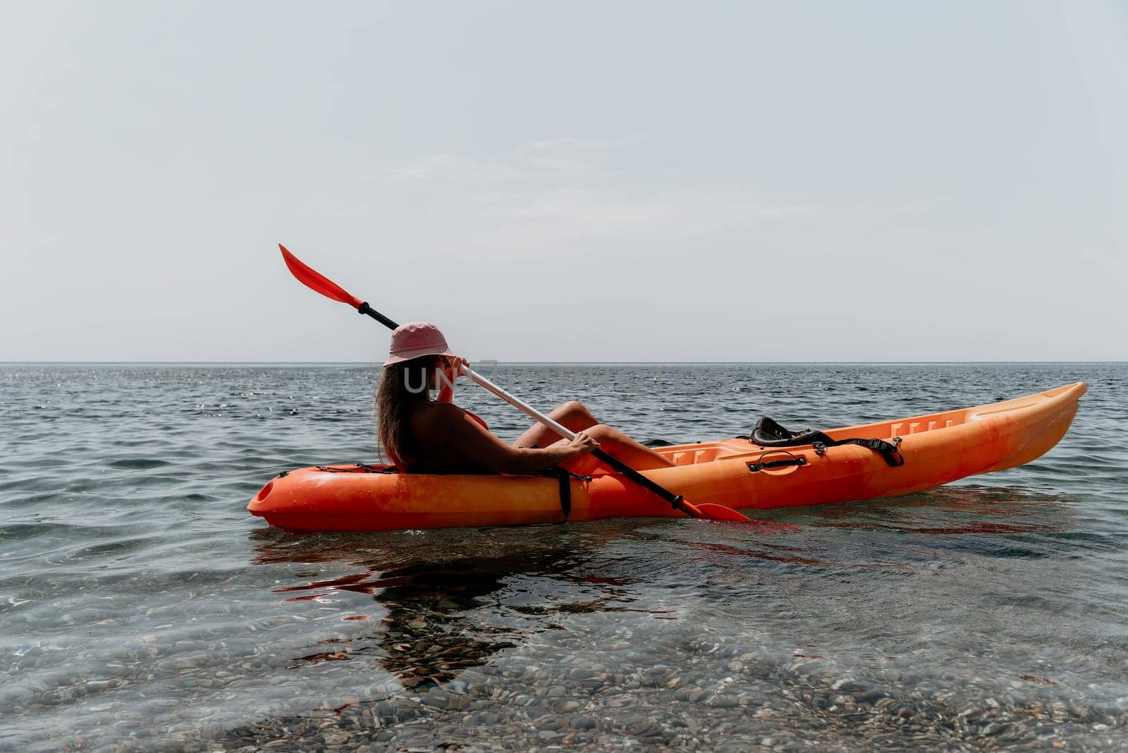 Happy smiling woman in kayak on ocean, paddling with wooden oar. Calm sea water and horizon in background