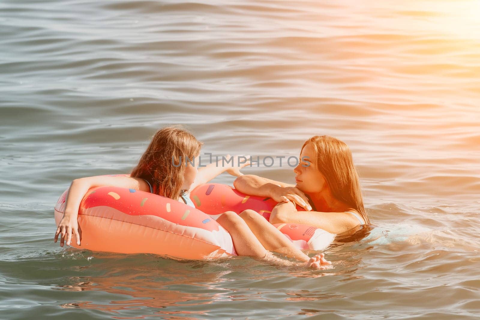 Two young women relax and chat while floating on a donut-shaped inflatable in the ocean.