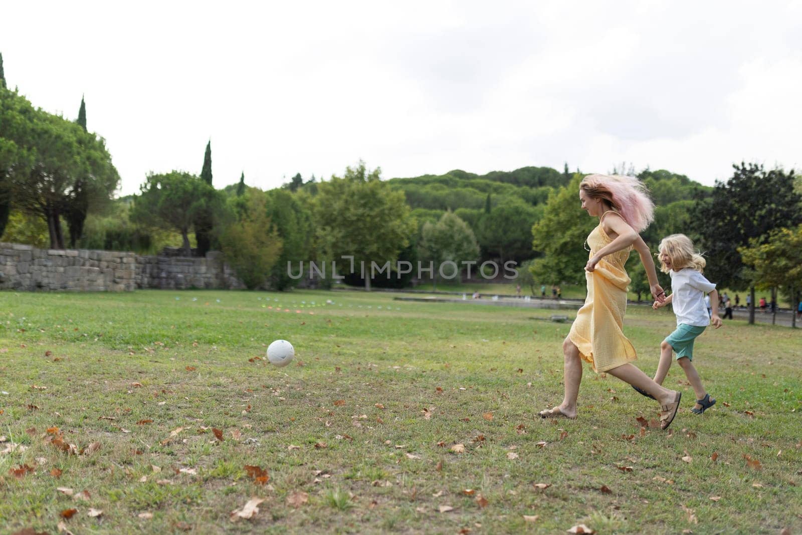Mother and her son are running after a soccer ball while playing together in a park
