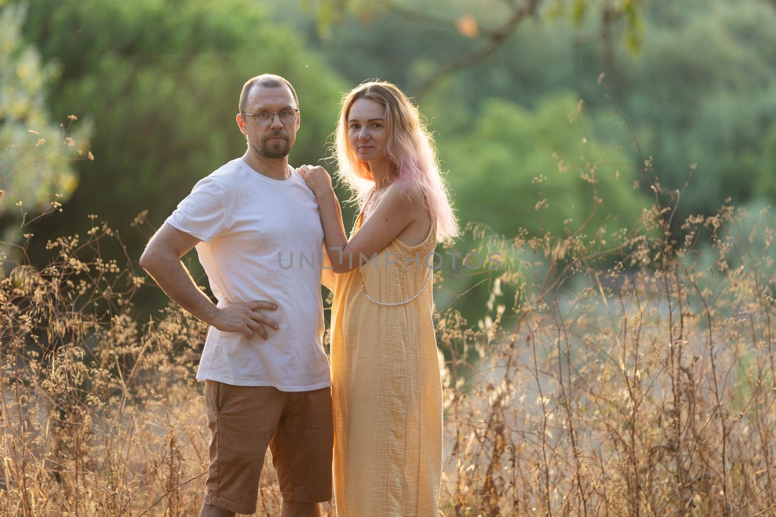 Man and a woman are posing in a field at golden hour