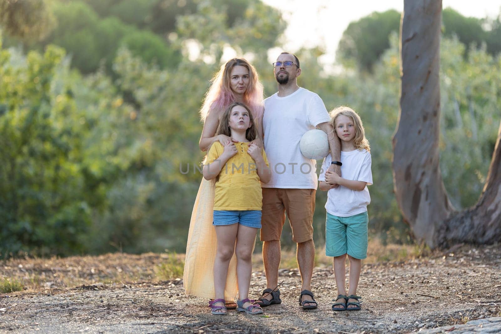 Family of four is posing together in a park while holding a volleyball