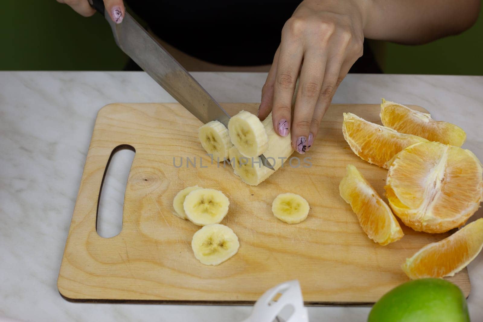 Girl cuts banana into pieces for easy blending while preparing sports drink from fruits. Healthy tonic smoothie for healthy lifestyle