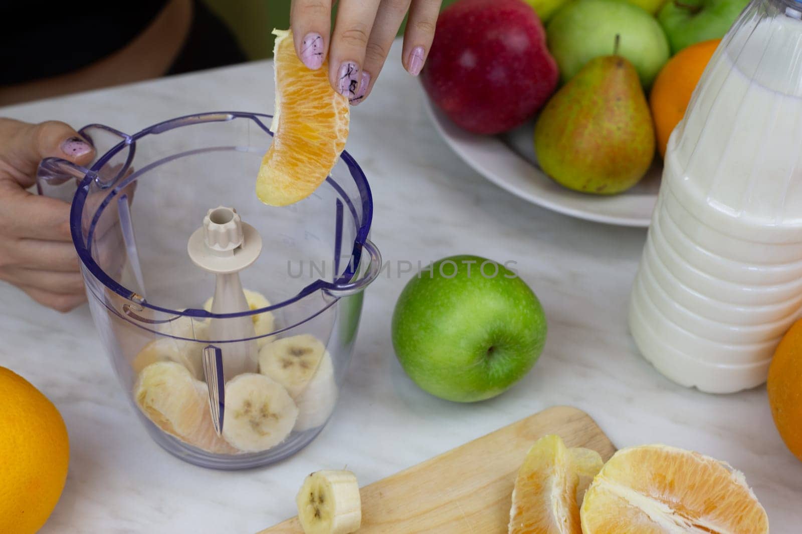 Woman hand lowers orange into blender container while making sports cocktail with milk at home. Boosting immunity and vitamins in the body with healthy drink