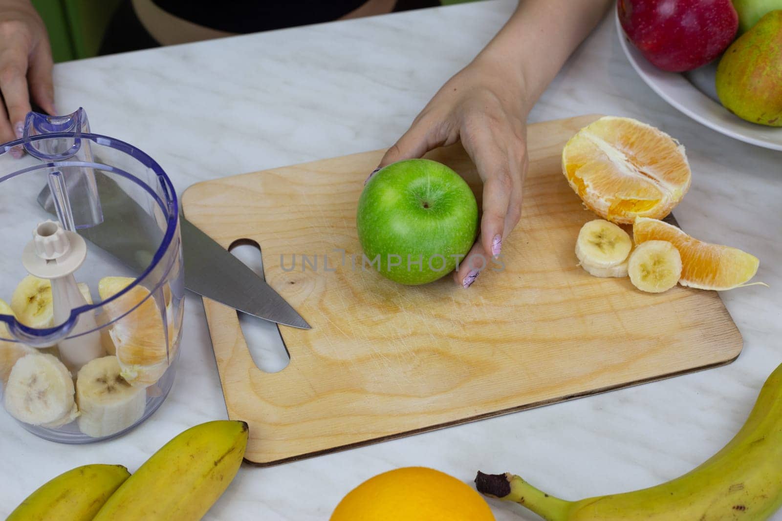 Girl cuts juicy green apple on board in kitchen while preparing sports drink in blender according to recipe, healthy cocktail with vitamins at home