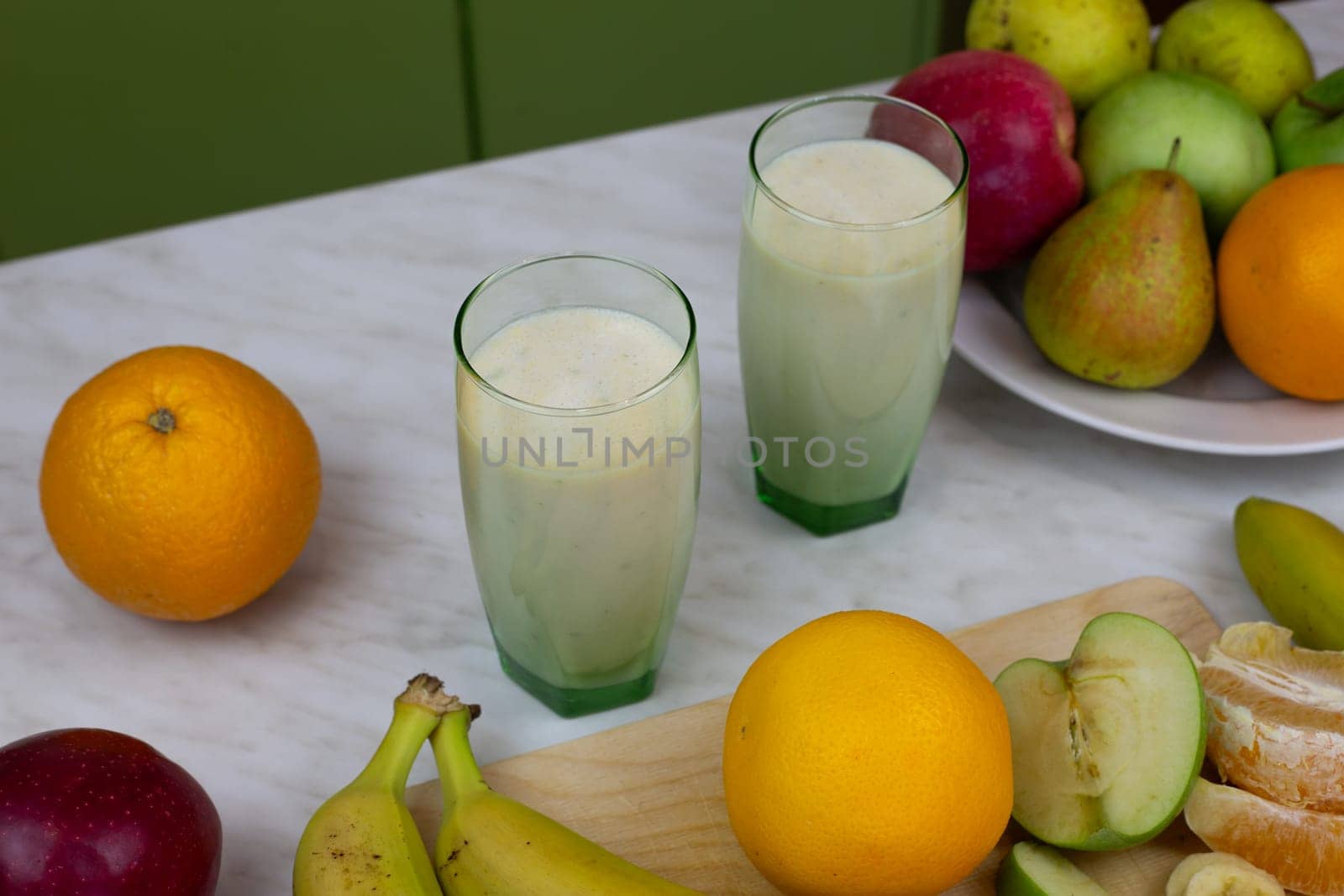 Two glasses with milkshake with vitamins on table with fruits. Ready made sports drink for improving health, refreshing drink with fruits and milk to boost vitamins