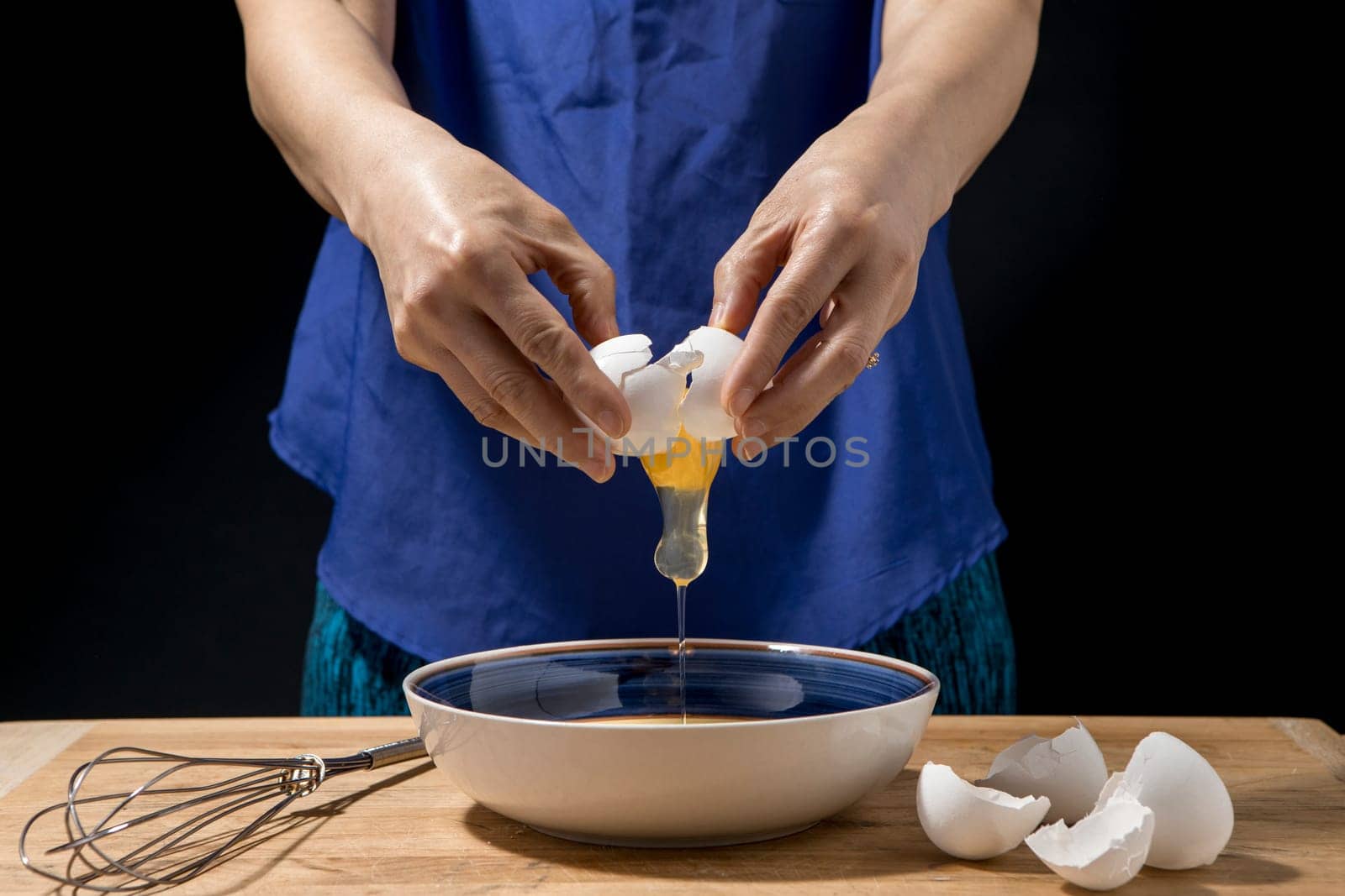 A woman cracks open and egg and the yolk falls to the bowl.