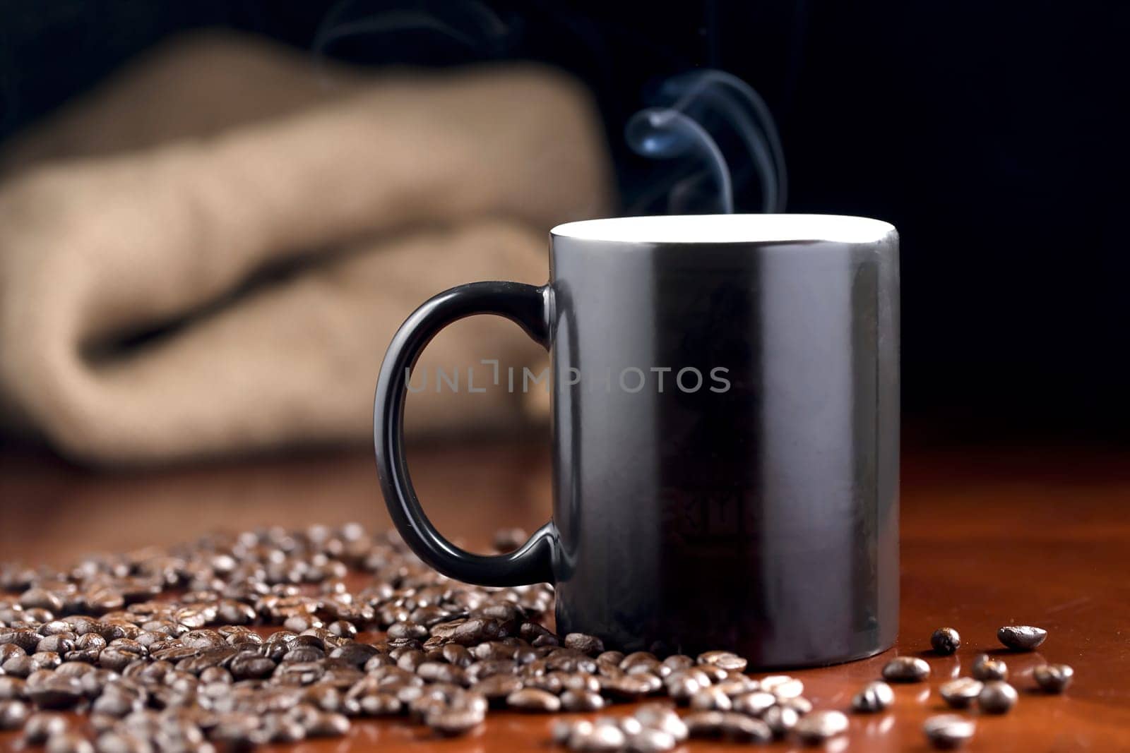 A studio photo of steaming coffee in a cup and coffee beans.