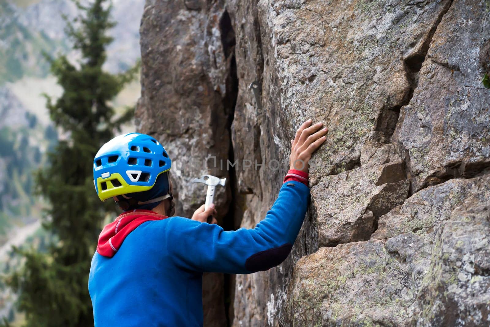 Young man checks the strength of the relief with a hammer, ..is engaged in extreme sports, an active lifestyle, climbs a mountain, a rock with equipment, wearing a helmet, with a rope and carabiners.