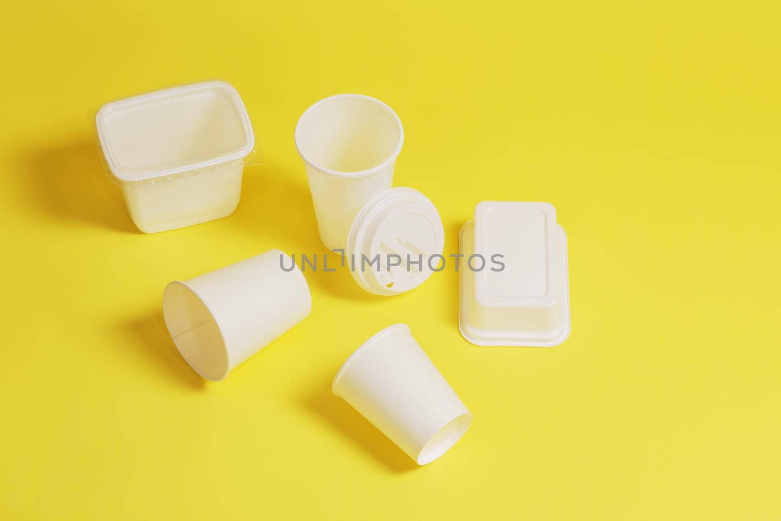 Disposable, white plastic cups with a lid, containers, boxes, on a yellow paper background.