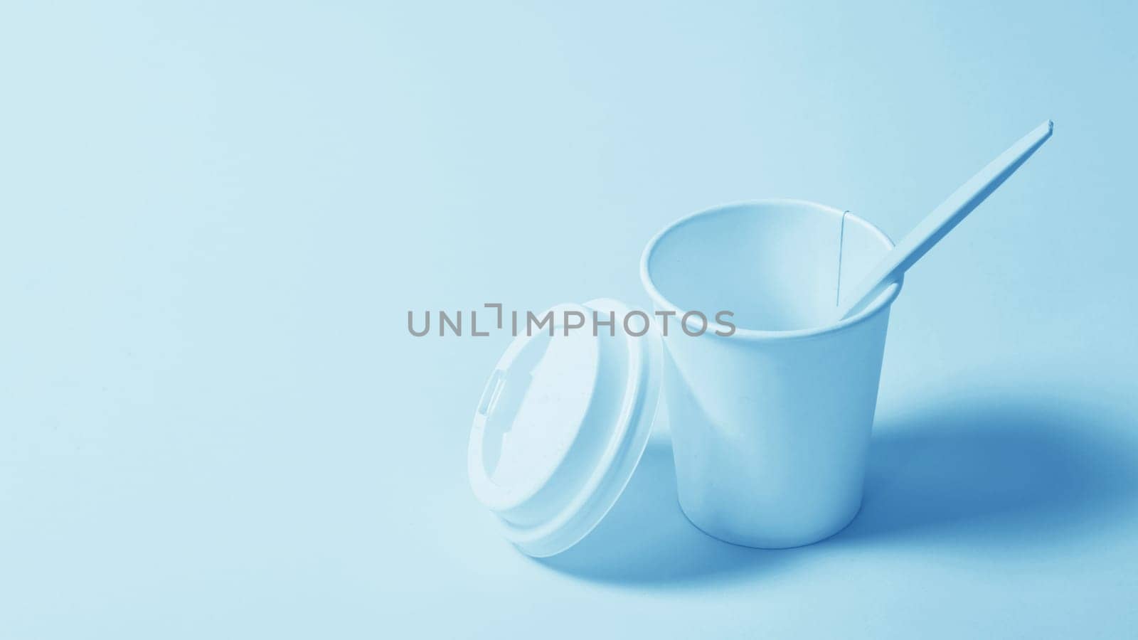 Disposable paper cup with a plastic lid and a plastic spoon on a blue paper background.