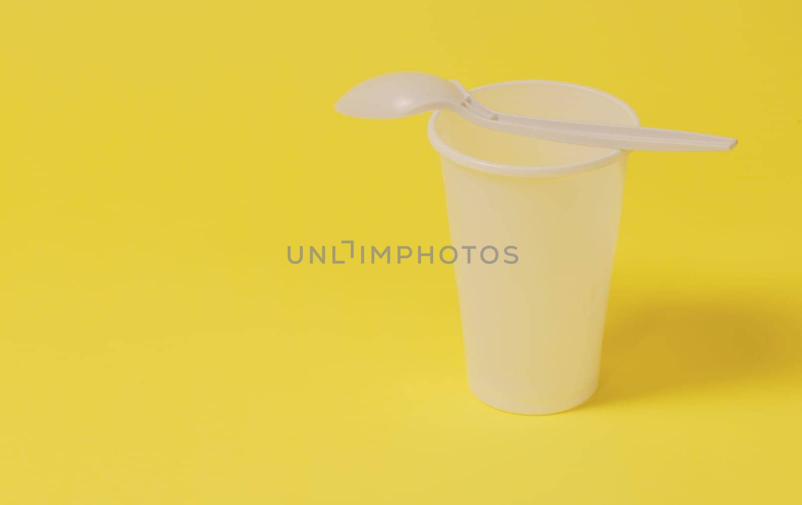 A plastic glass with a spoon lying on it on a yellow paper background.