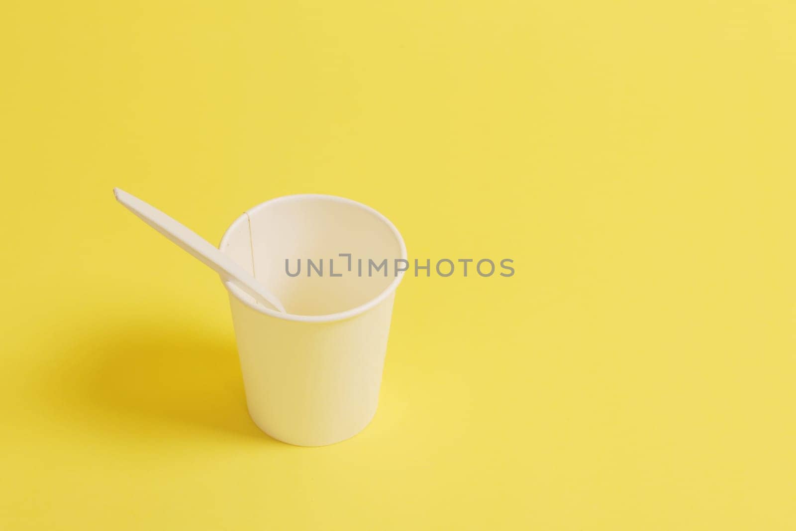 Disposable paper cup with spoon on a yellow background.