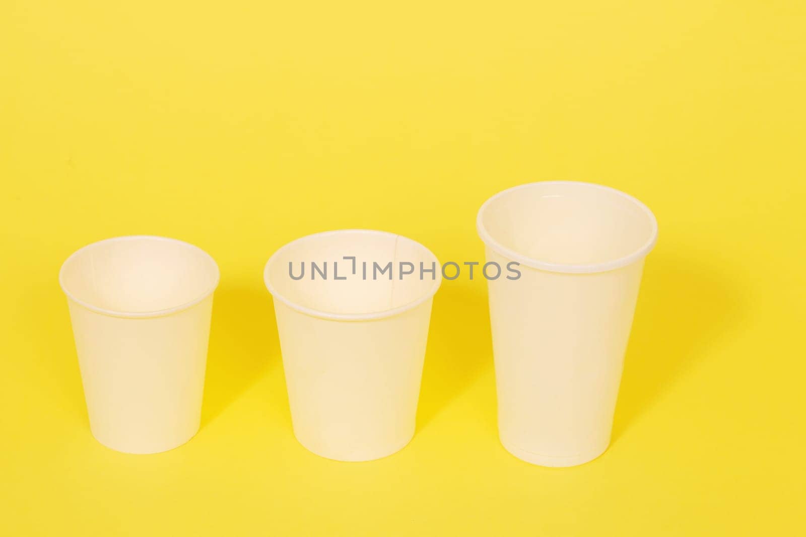 Three white plastic disposable cups on a yellow paper background.