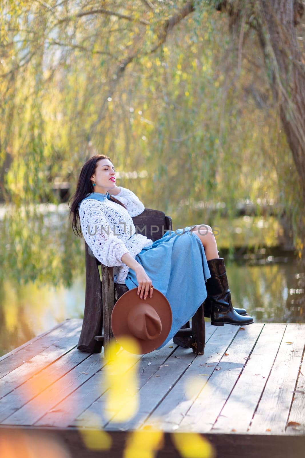 Autumn lake woman. She sits by a pond on a wooden pier in autumn and admires nature. The concept of tourism, weekends outside the city