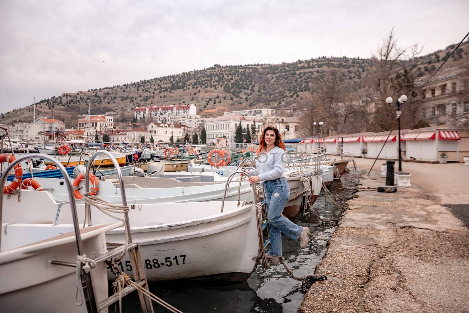 A woman stands in front of a row of boats, some of which have orange life preservers on them. The scene is peaceful and serene, with the boats and the woman creating a sense of calmness and relaxation