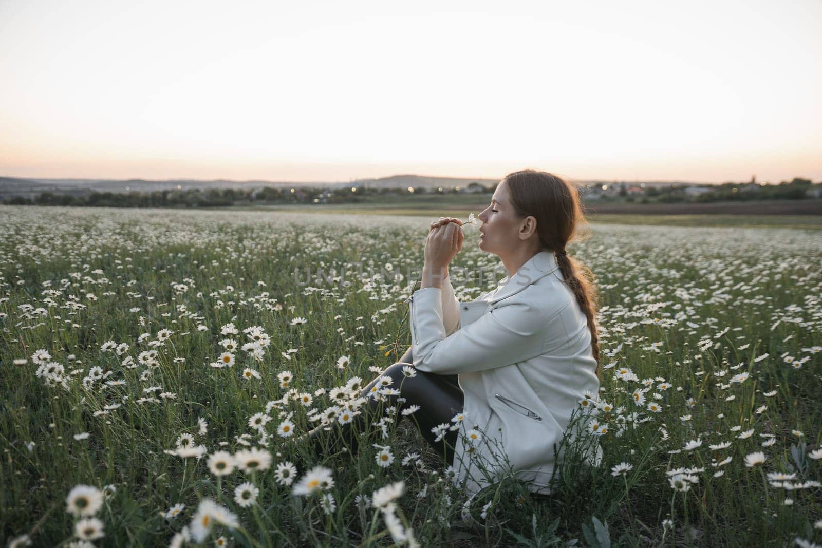 A woman is holding a flower and smelling it. Concept of peace and tranquility, as the woman is surrounded by nature and taking a moment to appreciate the beauty of the flower