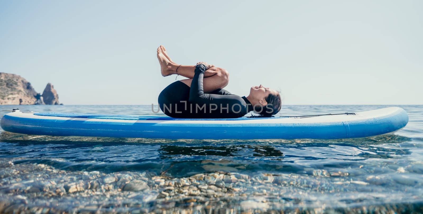 Woman sup yoga. Middle age sporty woman practising yoga pilates on paddle sup surfboard. Female stretching doing workout on sea water. Modern individual hipster outdoor summer sport activity