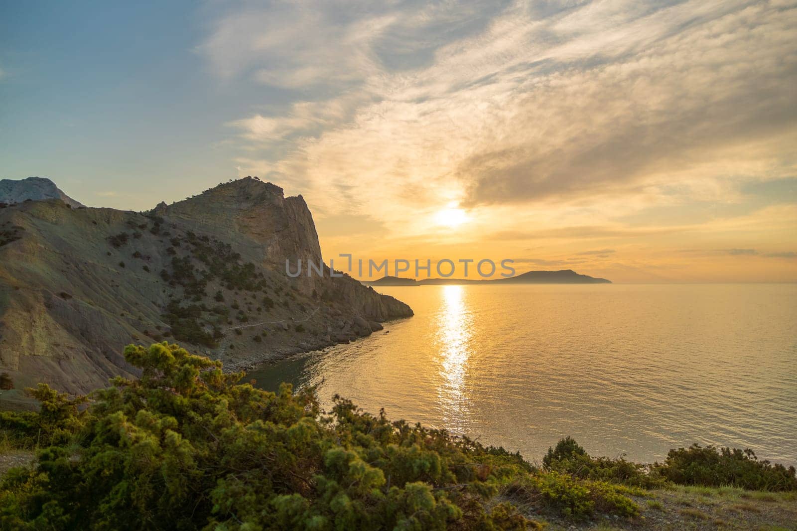 A beautiful sunset over the ocean with a rocky cliff in the background. The sky is filled with clouds, creating a serene and peaceful atmosphere