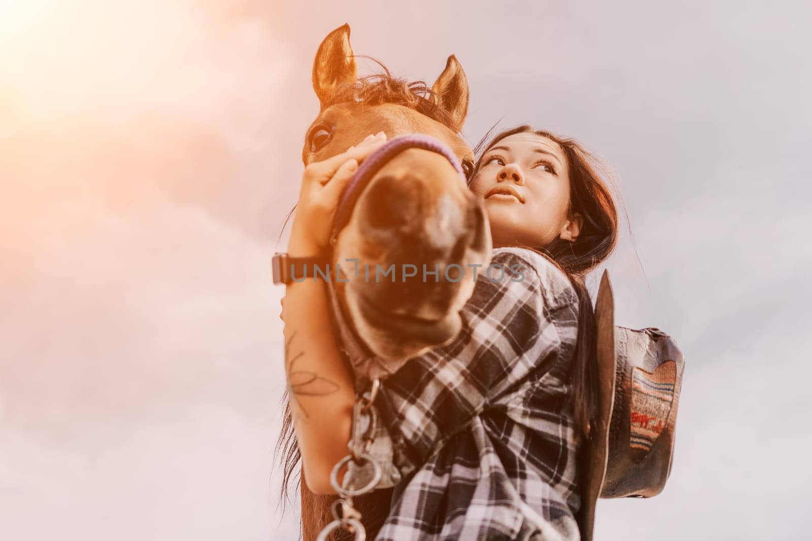 A young woman with long black hair and a plaid shirt holds a brown horse's face in her arms, their gazes meet, revealing a deep bond.