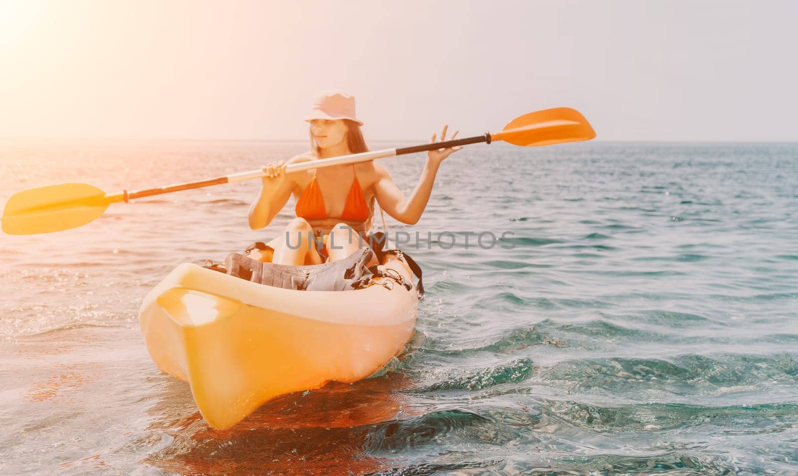 Happy smiling woman in kayak on ocean, paddling with wooden oar. Calm sea water and horizon in background