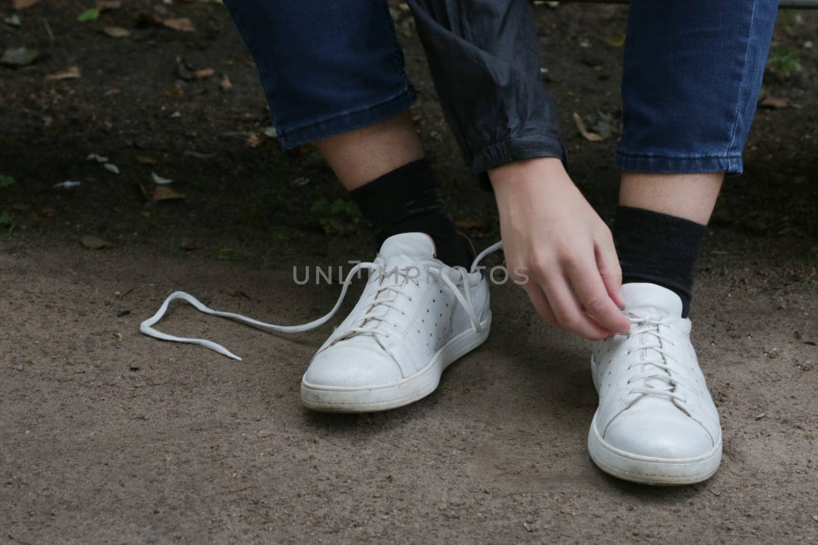 A young man's hand ties the laces on white sneakers close-up.