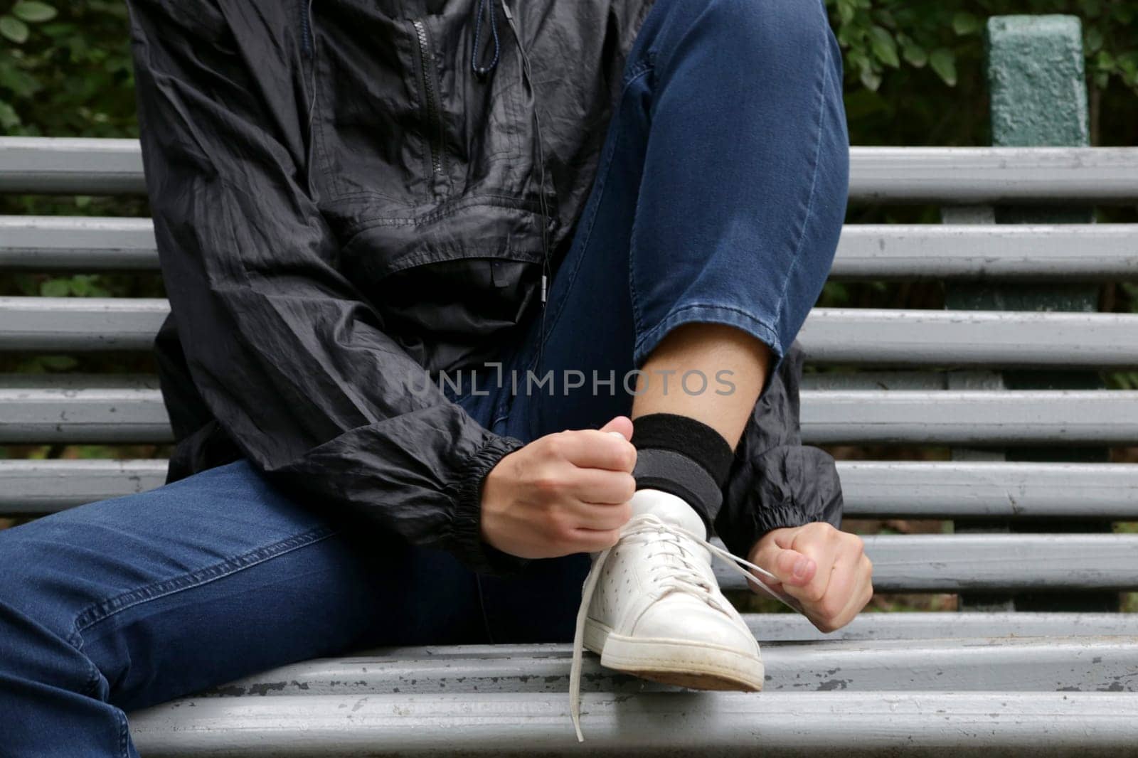 A boy in blue jeans and a blue windbreaker ties his laces on white sneakers.