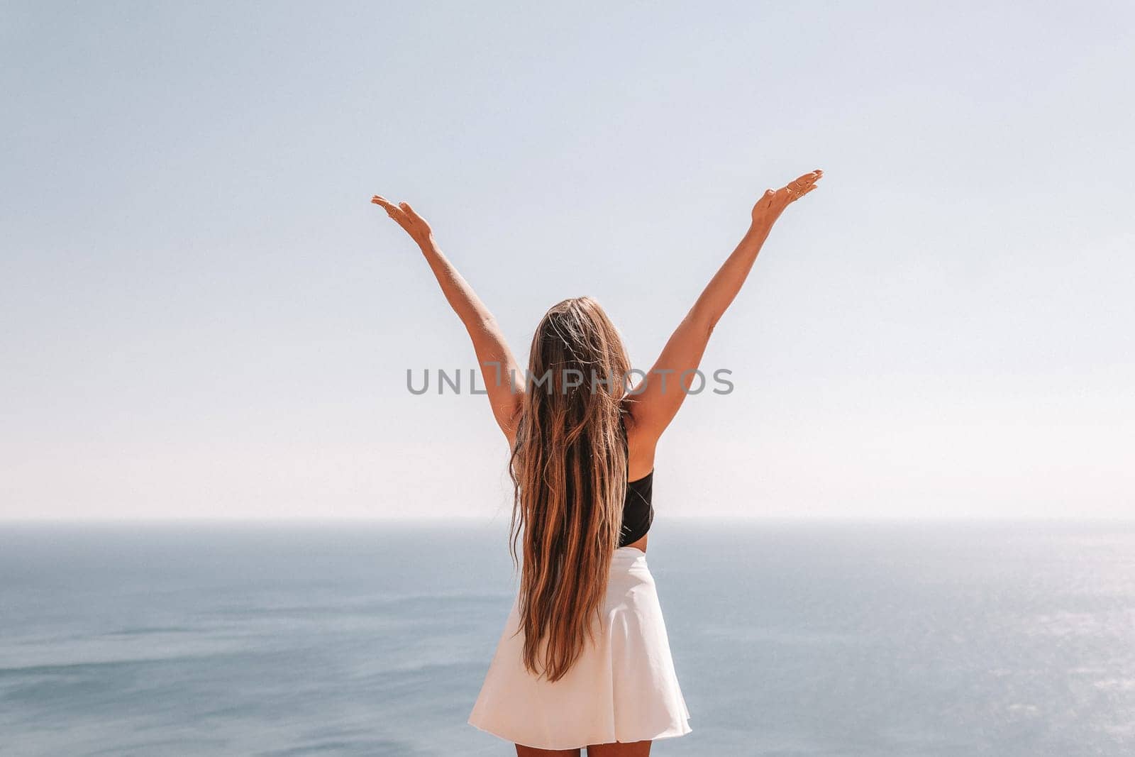 A woman with long hair stands on a beach, arms raised in the air, and the ocean is in the background