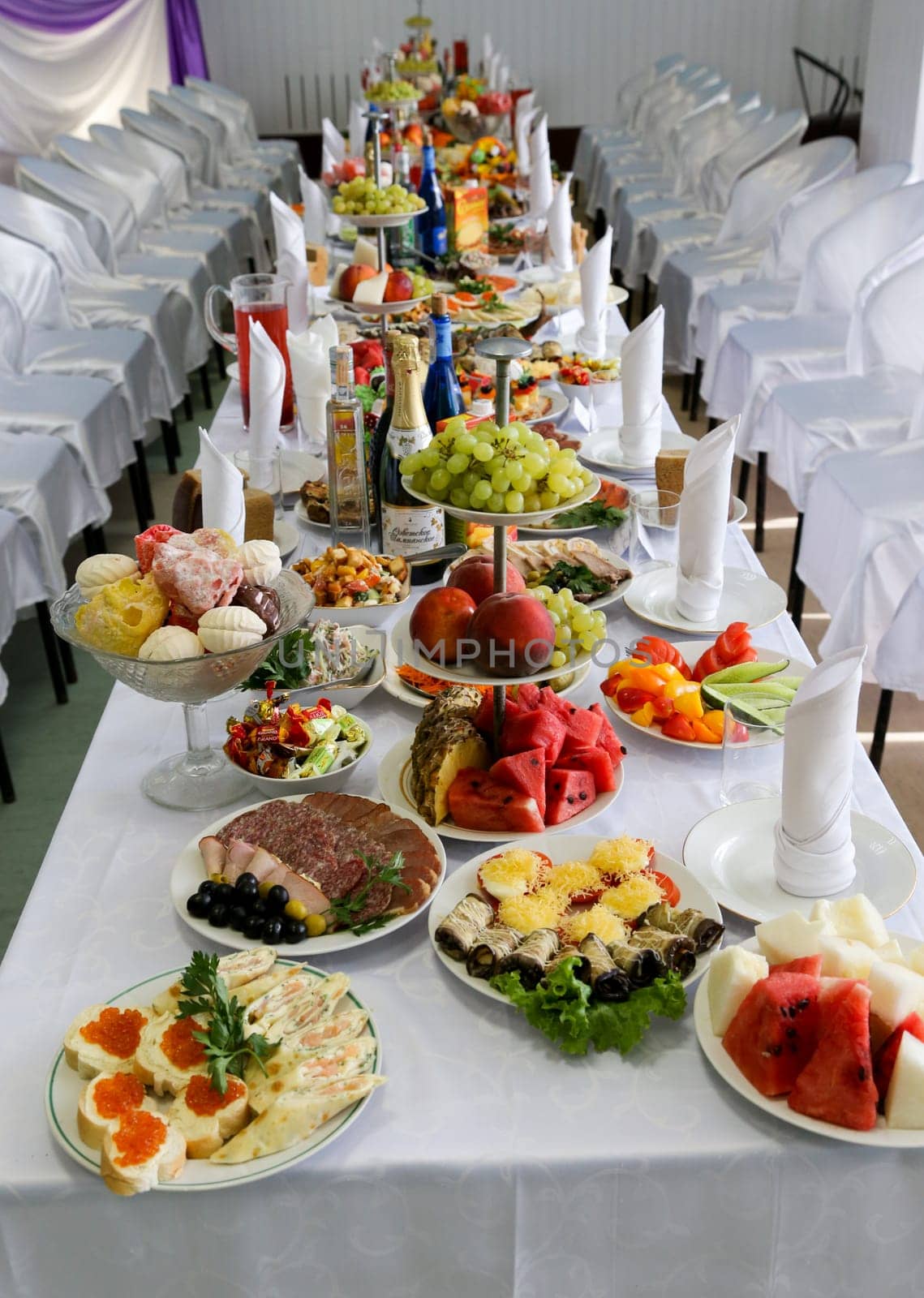 Wedding table covered with a white tablecloth with a variety of beautiful food dishes, white chairs.
