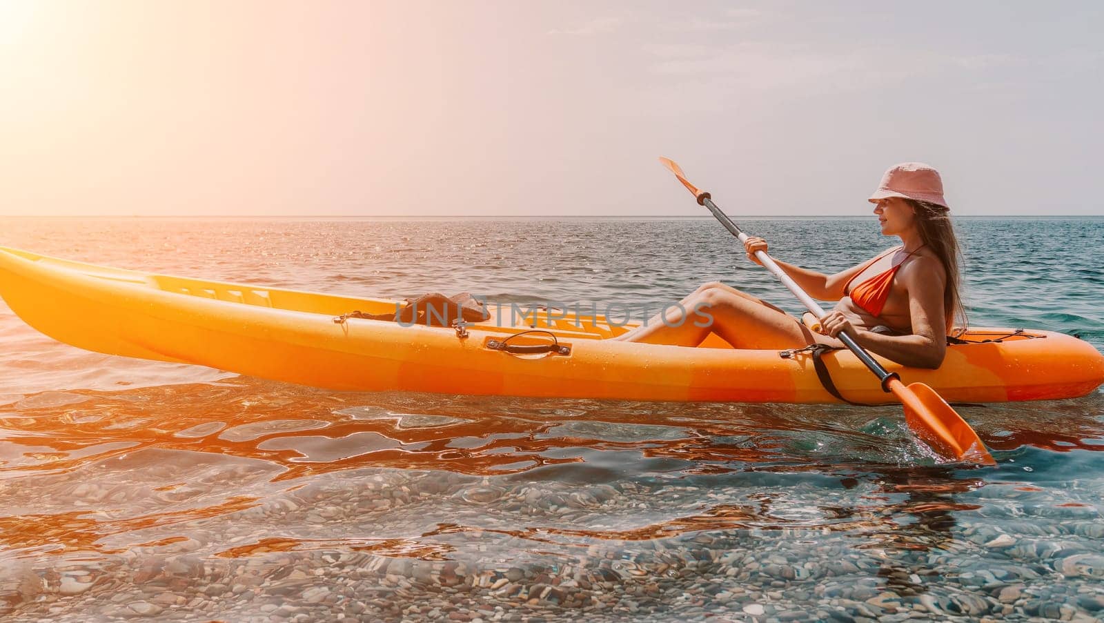 Happy smiling woman in kayak on ocean, paddling with wooden oar. Calm sea water and horizon in background