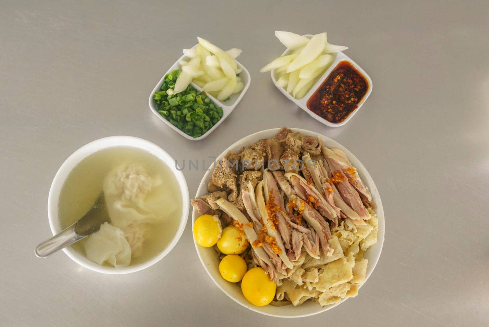 A bowl of Mie Ayam with various toppings, including shredded chicken, meatballs, egg, and vegetables. Served with a separate bowl of soup and condiments.