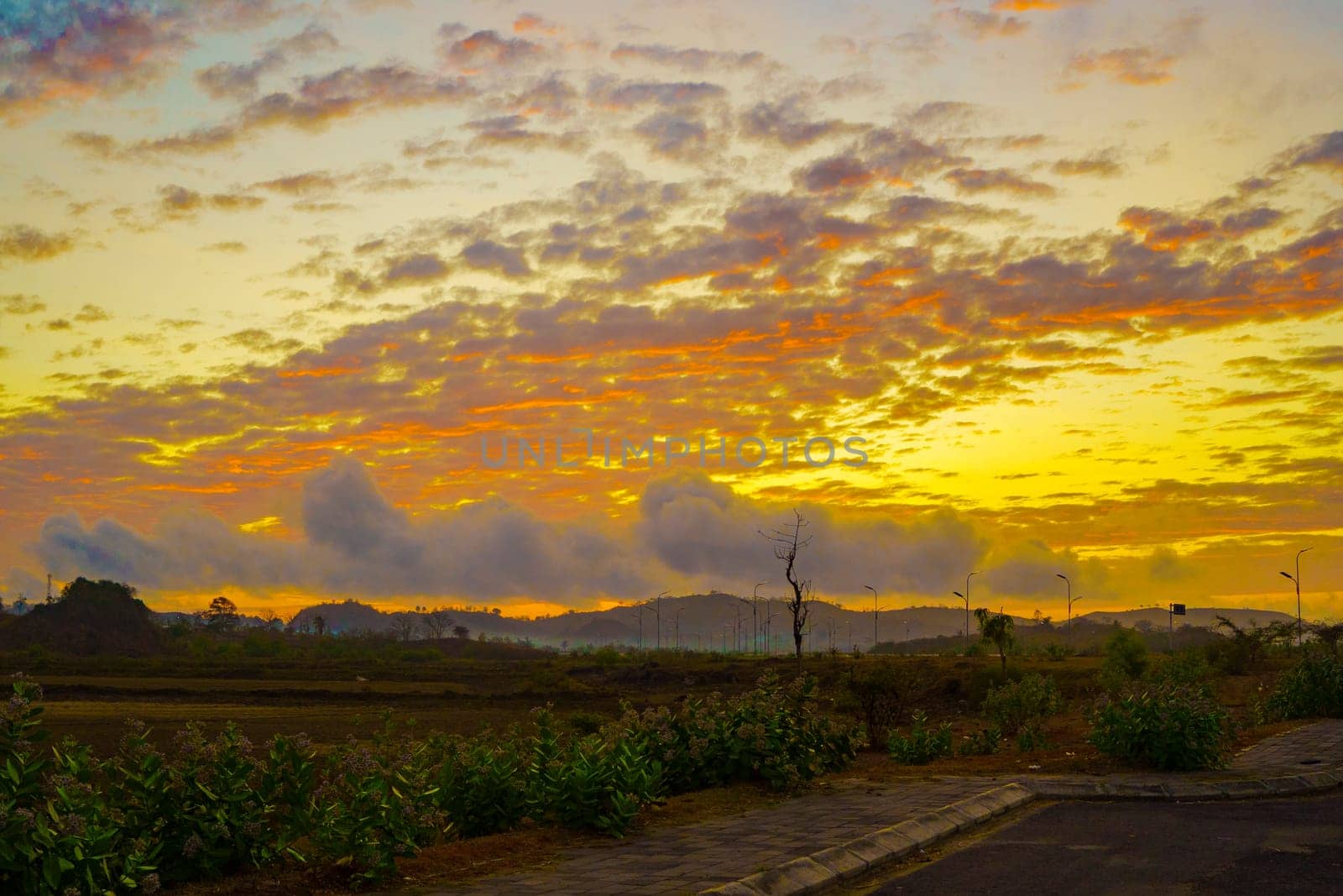 A breathtaking sunset paints the sky in vibrant hues of orange and pink, casting a warm glow over a vast landscape near Mandalika.