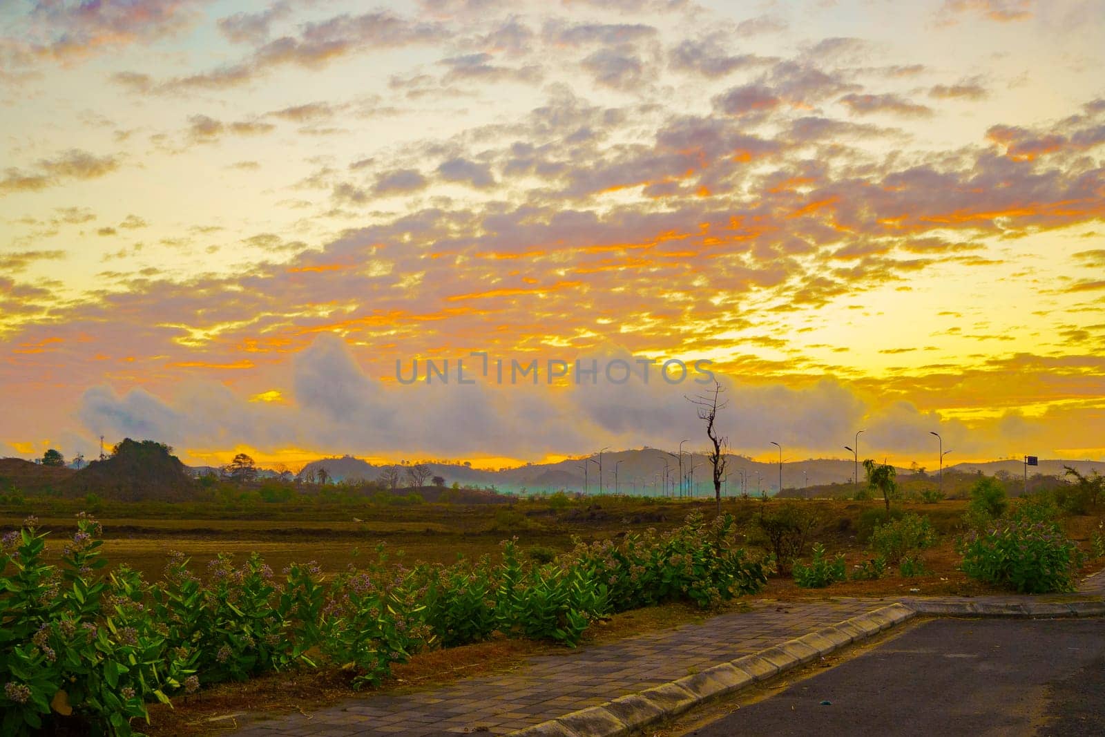 A breathtaking sunset paints the sky in vibrant hues of orange and pink, casting a warm glow over a vast landscape near Mandalika.