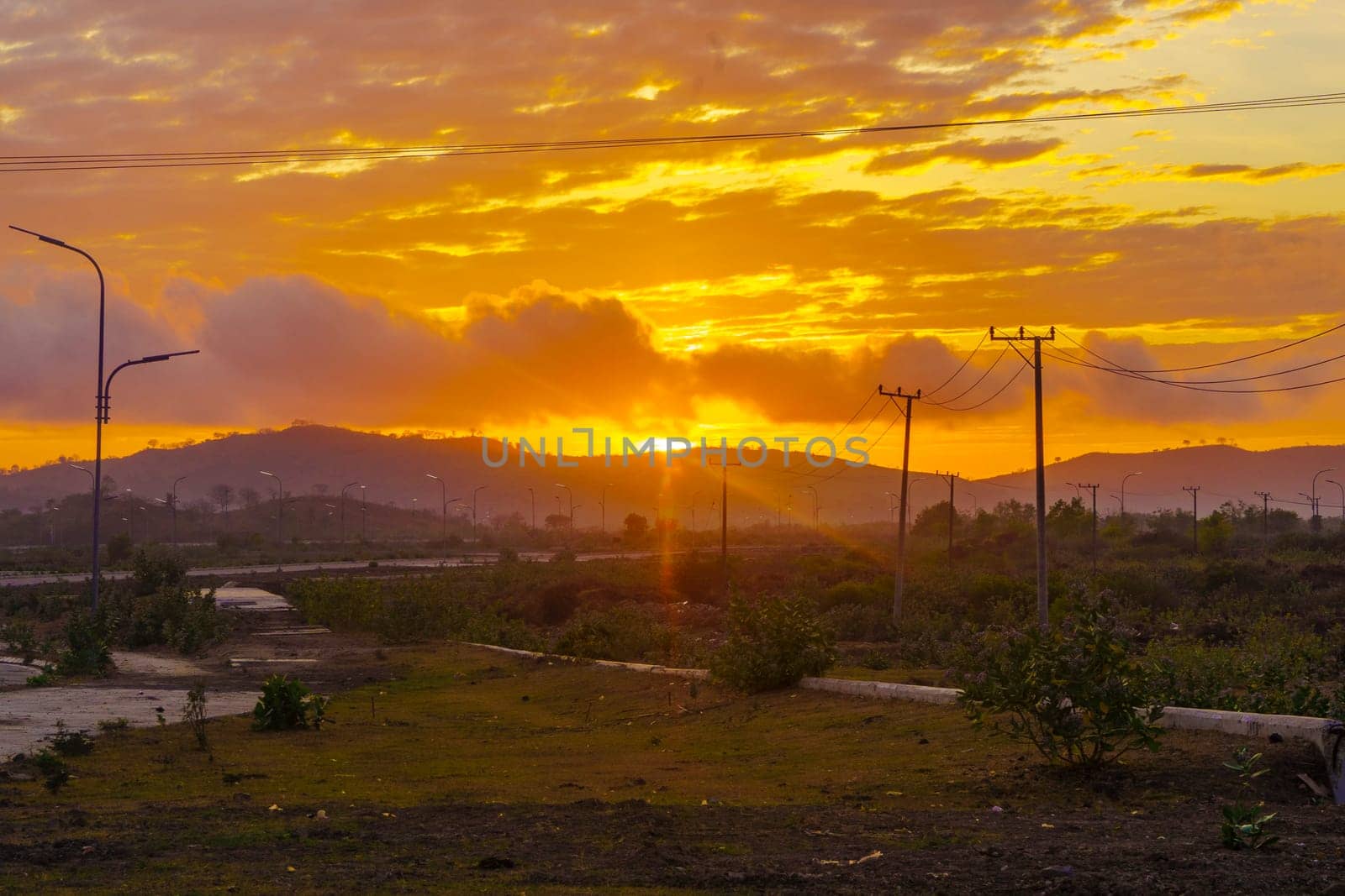 A breathtaking sunset paints the sky in vibrant hues of orange and pink, casting a warm glow over a vast landscape near Mandalika.